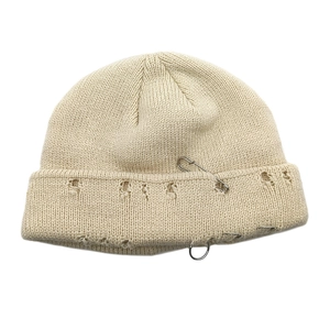 Detail of beige knit beanie featuring street style distressed holes and metal pin accents
