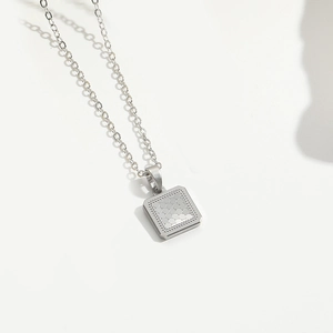 Detail shot of a silver square pendant with dot texture on a minimalist fine chain necklace