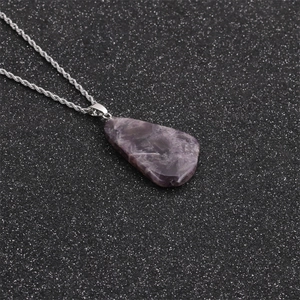 Détail d'un pendentif dent de loup en pierre violette avec chaîne torsadée sur fond noir