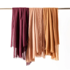 Close-up of lightweight linen scarves in deep red, peach, and mustard yellow with frayed edges