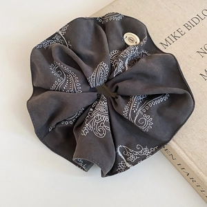 Detailed view of dark grey paisley fabric scrunchie with decorative brand button