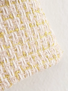 Close-up of elegant cream tweed fabric with golden metallic threads and woven texture