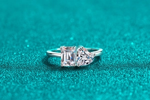 Macro shot of silver ring featuring emerald and heart cut stones on a glittery background