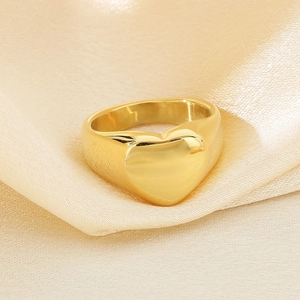 Close-up of polished 18K gold heart ring displayed on luxury champagne satin fabric