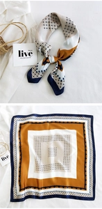 Detail of geometric navy and yellow silk scarf styled on a white shirt and straw bag