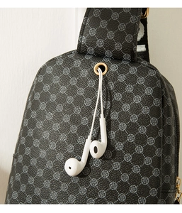 Close-up of black crossbody bag with clover pattern and functional gold earphone port