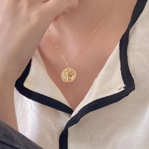 Detail of vintage gold coin pendant necklace with lion relief on white sweater