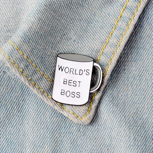 Close-up of World's Best Boss coffee mug enamel pin on a blue denim jacket pocket