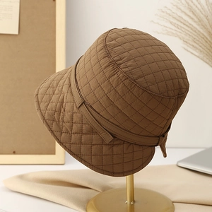 Quilted brown bucket hat with adjustable tie displayed on a vintage gold hat stand