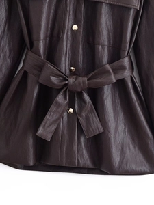 Detail of a dark brown faux leather coat featuring a gold button and tied waist belt