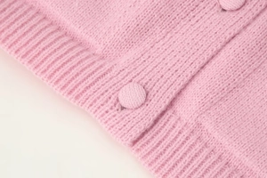 Close-up of pink knit cardigan showing fabric covered buttons and ribbed texture