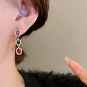 Close-up of dangling earrings featuring oval purple, green, and red zircon gemstones