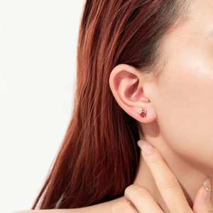 Close-up of minimalist sterling silver stud earring with a red zircon on human ear