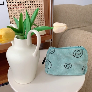 Detail of mint green corduroy makeup bag with black embroidered smiley face design