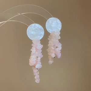 Detail view of pink crystal stone earrings with bow tassels on a minimalist display