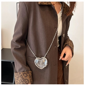 Detail of a clear heart-shaped acrylic mini bag with silver chain on model