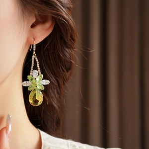 Detailed close-up of a long drop earring with zircon flower and green teardrop pendant