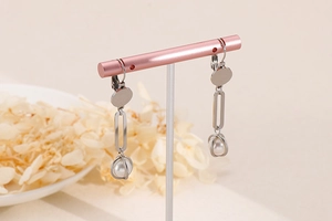 Detail of long pearl earrings with silver geometric links on a pink display stand