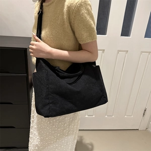 Black corduroy oversized tote bag with adjustable wide strap shown in a casual side view