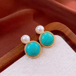 Vintage round pearl earrings with turquoise stone and golden bead edge on silk background
