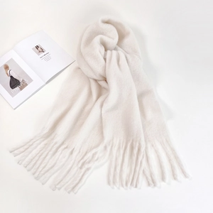 Detailed flat lay of soft white mohair scarf with tassels next to a fashion magazine