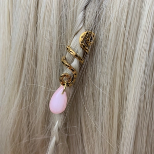 Close-up of golden spiral hair ring with a pink crystal droplet on blonde braids