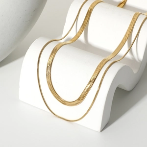 Detail view of double-layered gold snake bone chain necklaces on a white stand