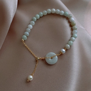 Detailed close-up of jade beads and white pearl bracelet on elegant champagne silk fabric