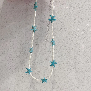 Detail of white seed bead necklace with blue starfish pendants and silver extension chain