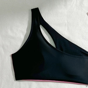Detail of black one-shoulder bikini top with metallic pink hem and cutout design