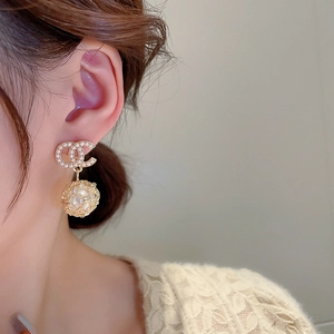 Detailed close-up of gold C-shaped earrings with woven metal balls and pearls