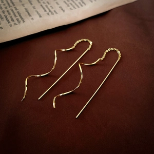 Elegant gold wavy chain tassel pull-through earrings on a vintage textured fabric