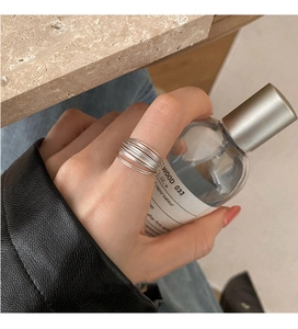 Close-up of minimalist layered silver rings on model hand holding perfume bottle