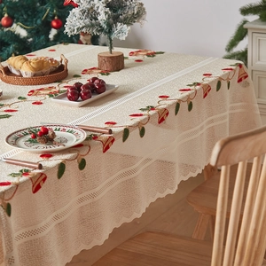 Detailed embroidery of Christmas bells and holly leaves on beige lace tablecloth