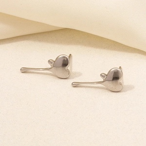 Macro shot of silver heart stud earrings with long curved tails on beige fabric background
