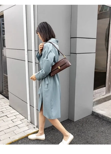Brown leather baguette shoulder bag with gold buckle worn with a stylish trench coat