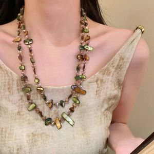 Detail of vintage layered necklace featuring green and amber shell beads on a model
