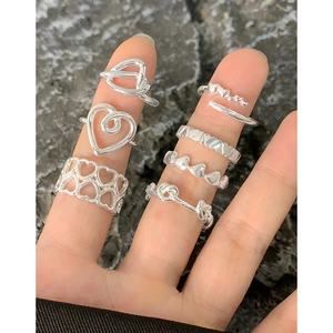Minimalist silver heart ring set with knot and spiral designs on stone background