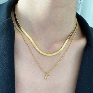 Macro detail of gold-plated snake chain and H-shaped diamond-encrusted pendant necklace