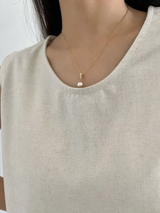 Close-up of a white pearl pendant necklace with diamond accents on a gold chain
