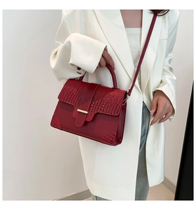 Detail einer rotbraunen Handtasche mit Krokostruktur und elegantem Metallverschluss