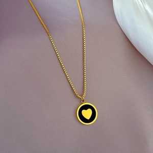 Detailed macro shot of a gold heart pendant with black enamel on a box chain