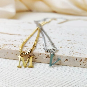 Detailed shot of gold and silver initial M and V pendants on elegant box chains