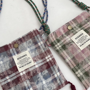 Close-up of small plaid crossbody bags with fringe, woven rope straps and magnetic metal buckle