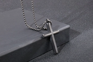 Close-up of matte black stainless steel cross pendant on dark geometric display stand