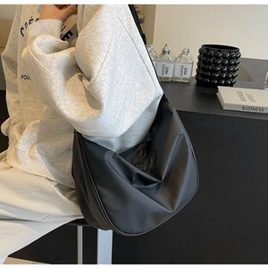 Close-up of a large black matte crossbody bag worn by a model in a minimalist lifestyle setting