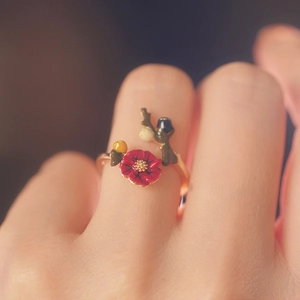Close-up of a gold open ring featuring a red flower design and green leaf details