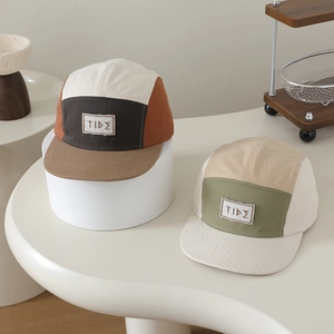 Dettaglio di cappellini da baseball in tela bicolore con patch logo TIDΣ su piedistalli