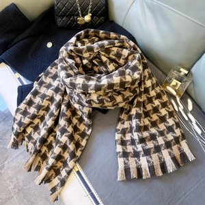 Detailed close-up of thick houndstooth knit scarf with fringes on a designer background