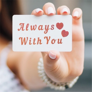 Macro shot of white card with pink glitter 'Always With You' lettering and heart icons